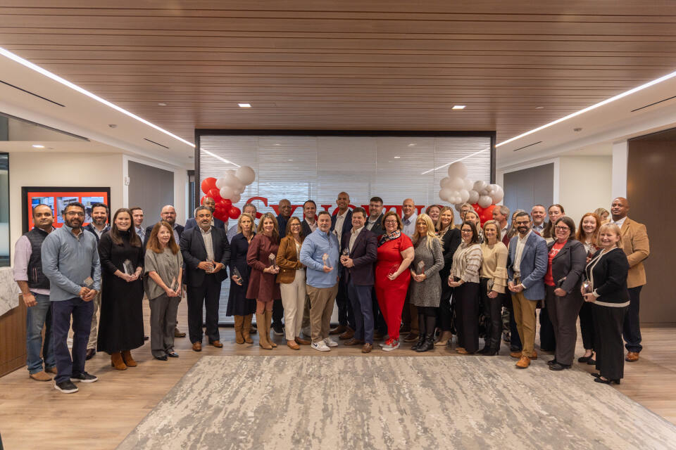 Group of Synovus Circle of Excellence Award winners standing together in a decorated office lobby with red, white, and gray balloons.