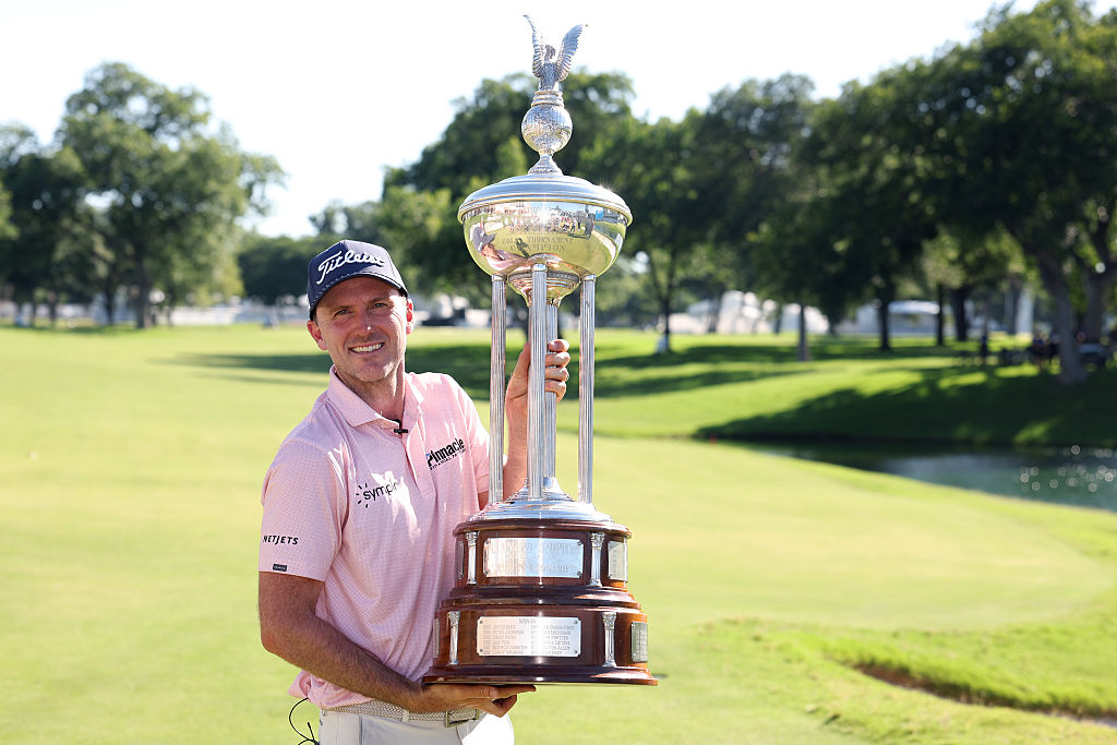 Russell Henley holding the Charles Schwab Challenge trophy on the golf course.
