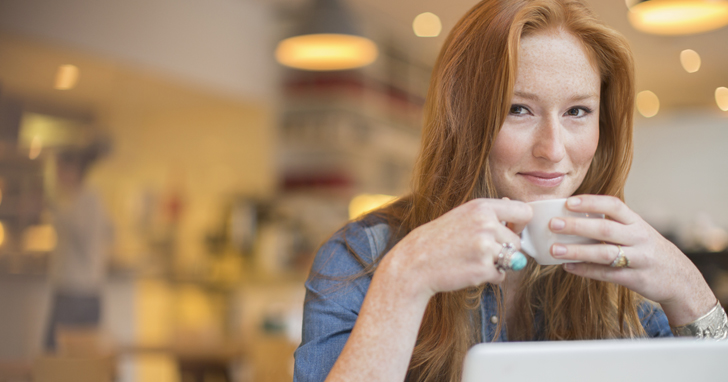 Young woman drinks a cup of coffee at her laptop