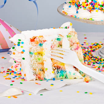 slice three layer confetti cake with white frosting and sprinkles on a plate