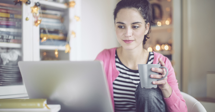 Young woman at laptop holding cup of coffee