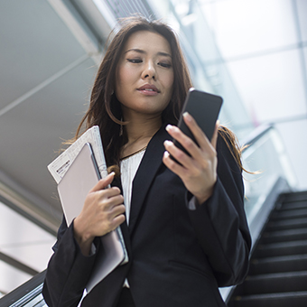 businesswoman on escalator glances at cell phone