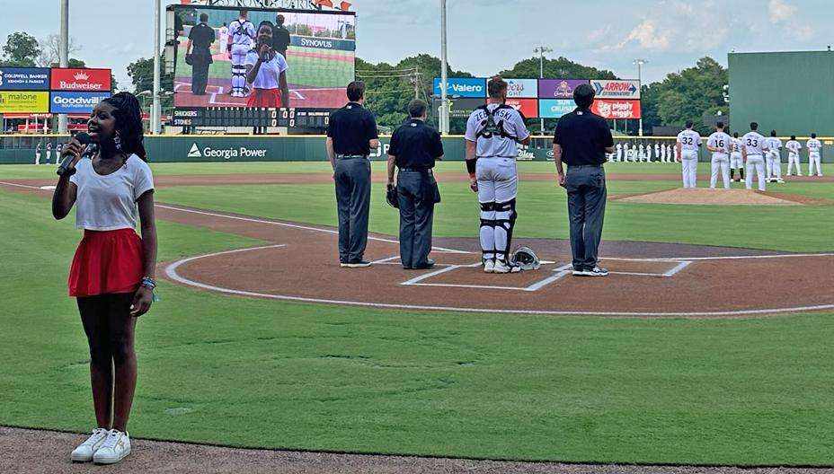 A young woman sings the national anthem behind home plate before the start of a Columbus Clingstones game at Synovus Park.